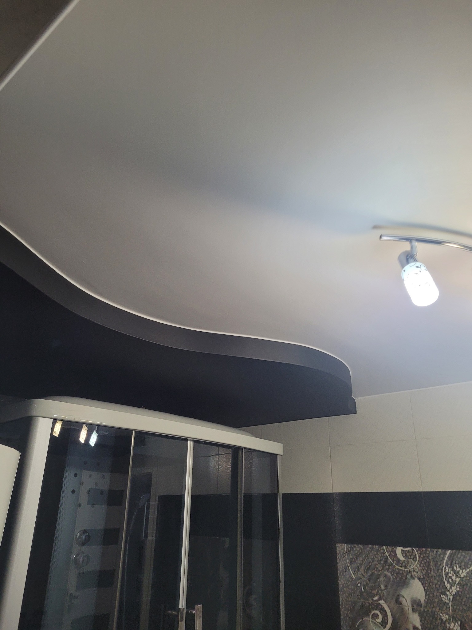 Wykończony sufit podwieszany w łazience z oświetleniem punktowym i kabiną prysznicową w tle, widok z dołu.