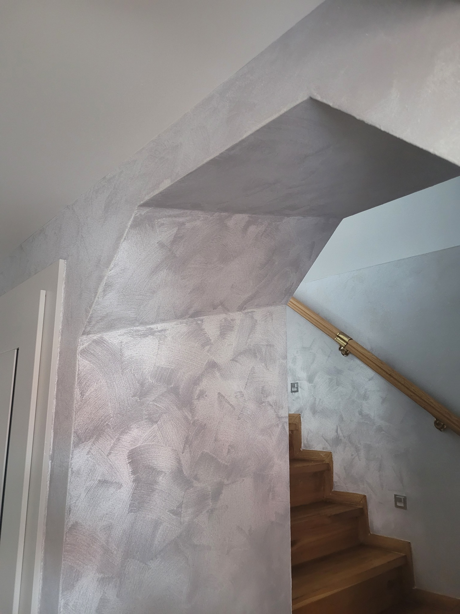 Ściana przy schodach pokryta dekoracyjną srebrzystą farbą z efektem przecierki, widoczny fragment schodów z drewnianą poręczą