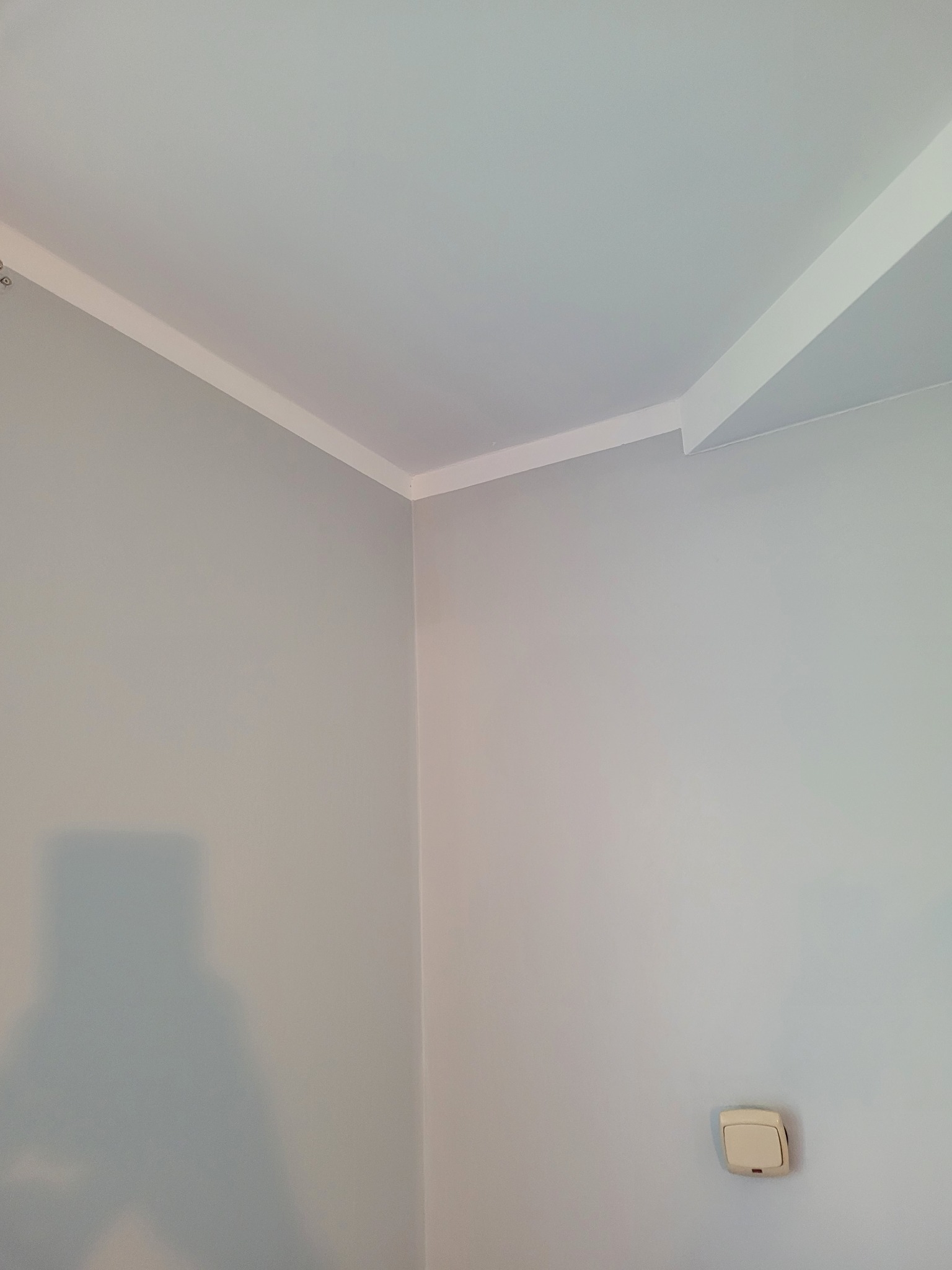 Świeżo pomalowane wnętrze w odcieniach szarości z białym wykończeniem sufitu i włącznikiem światła na ścianie.