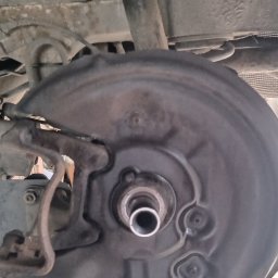 Carboost - Zdjęcie podwozia samochodu z widoczną tarczą hamulcową, elementami zawieszenia i fragmentem układu wydechowego. Widoczne ślady korozji i zabrudzenia.