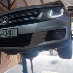 Srebrny samochód Volkswagen na podnośniku hydraulicznym podczas wymiany oleju, widoczny pojemnik na zużyty olej i klucz nasadowy obok.