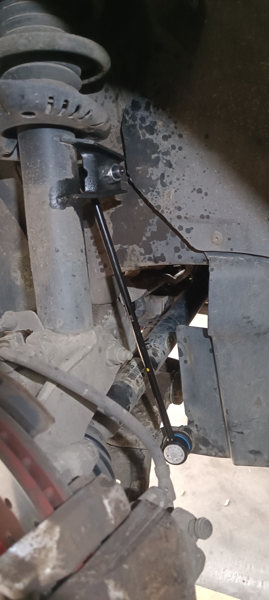 Nowy łącznik stabilizatora zamontowany w zawieszeniu samochodu, widoczne elementy zawieszenia i koła.