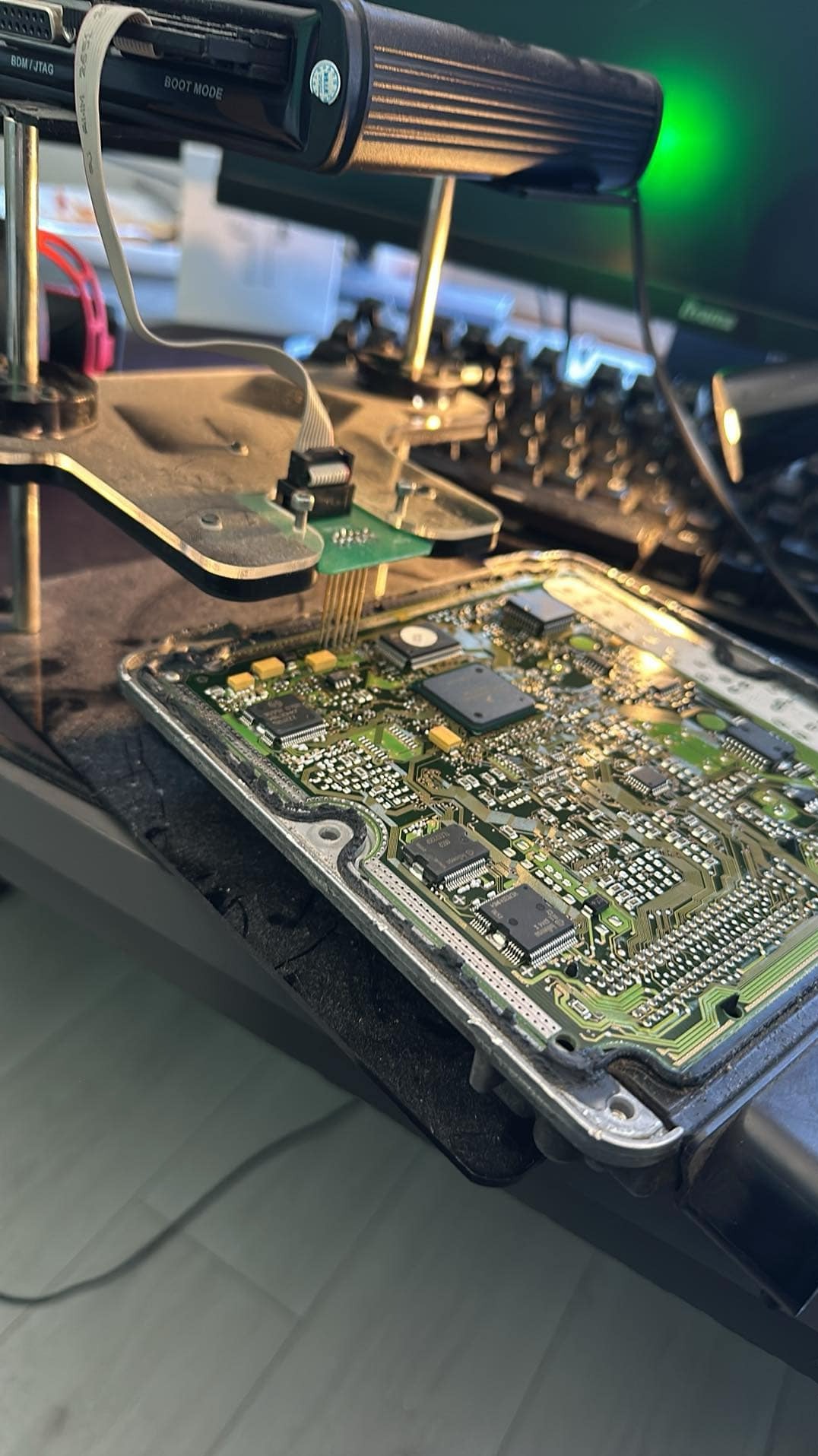 Elektroniczny moduł sterujący silnika (ECU) podłączony do programatora z napisem 'BOOT MODE' podczas diagnostyki lub programowania, widoczne układy scalone i złącza.