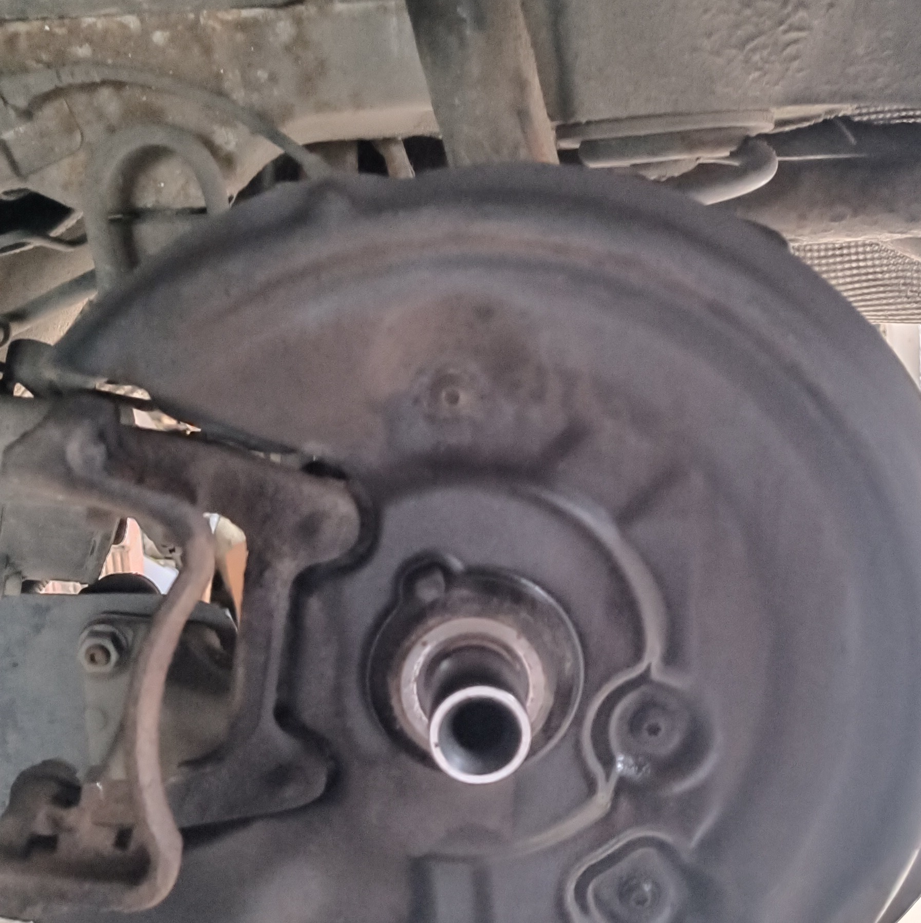 Zdjęcie podwozia samochodu z widoczną tarczą hamulcową, elementami zawieszenia i fragmentem układu wydechowego. Widoczne ślady korozji i zabrudzenia.