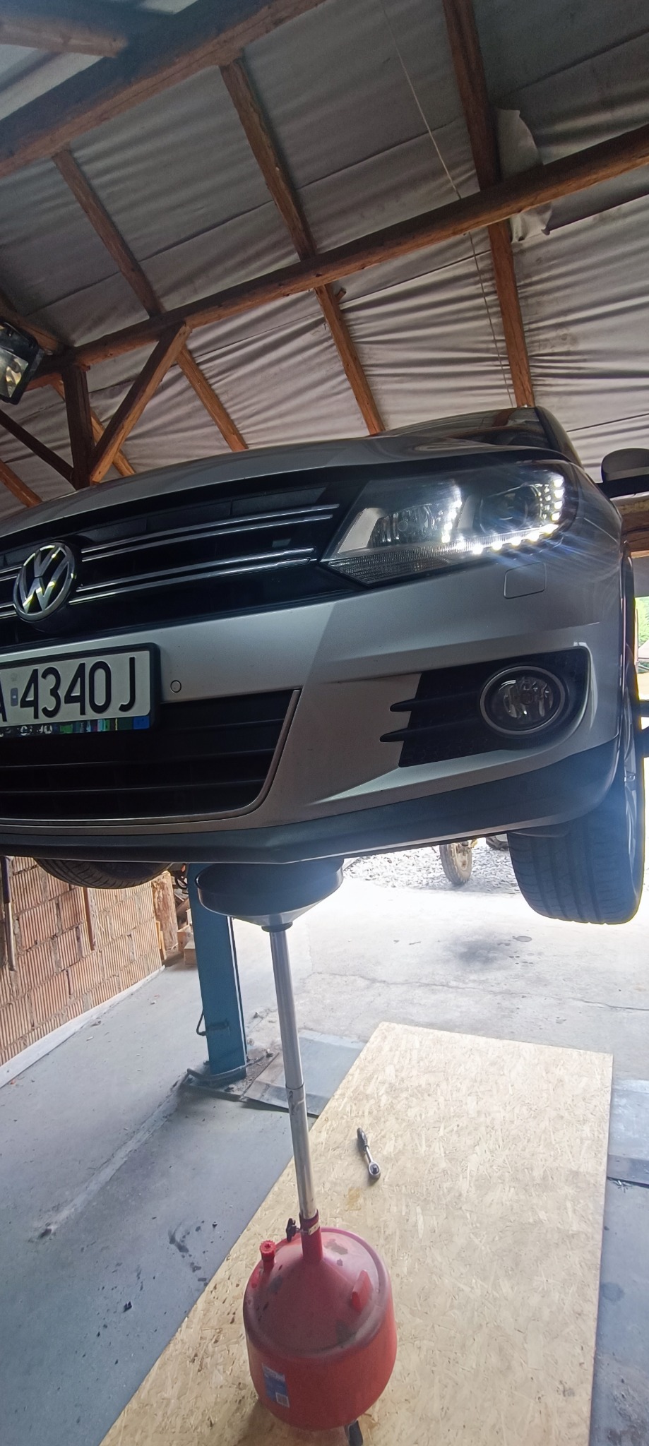 Srebrny samochód Volkswagen na podnośniku hydraulicznym podczas wymiany oleju, widoczny pojemnik na zużyty olej i klucz nasadowy obok.