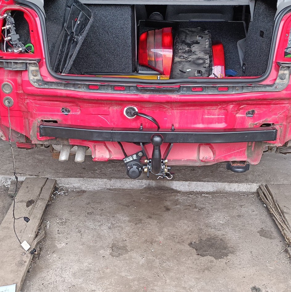 Czerwony samochód z zamontowanym hakiem holowniczym, widoczne elementy instalacji elektrycznej, otwarty bagażnik z częściami zamiennymi.