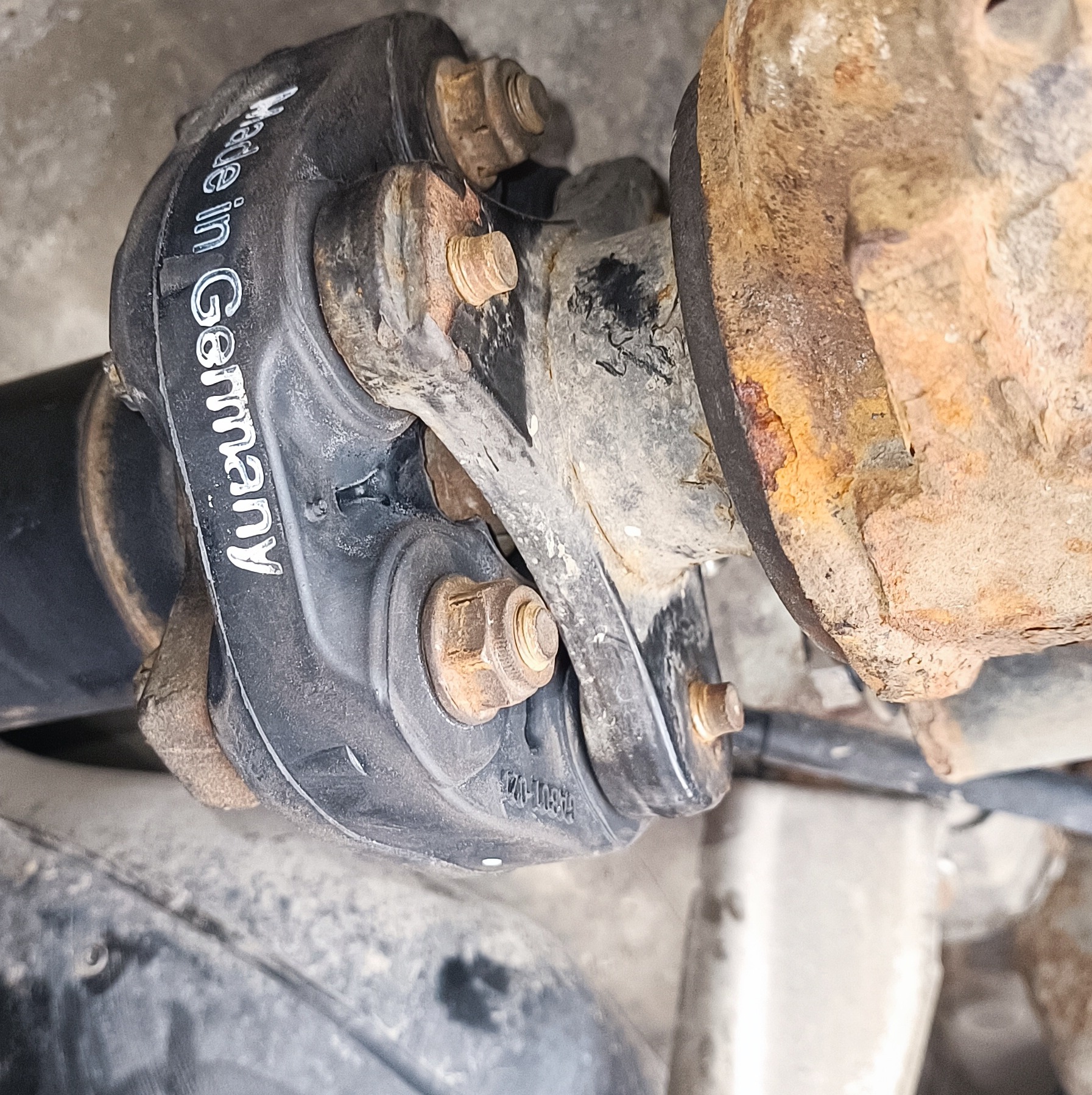 Gumowe sprzęgło elastyczne wału napędowego z napisem 'Made in Germany' połączone z zardzewiałym elementem metalowym, widoczne ślady korozji i zużycia.