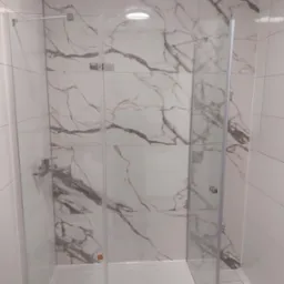 Kabina prysznicowa z marmurowymi płytkami, chromowana bateria i odpływ liniowy. Nowoczesna łazienka po remoncie, jasne wnętrze, minimalistyczny design.