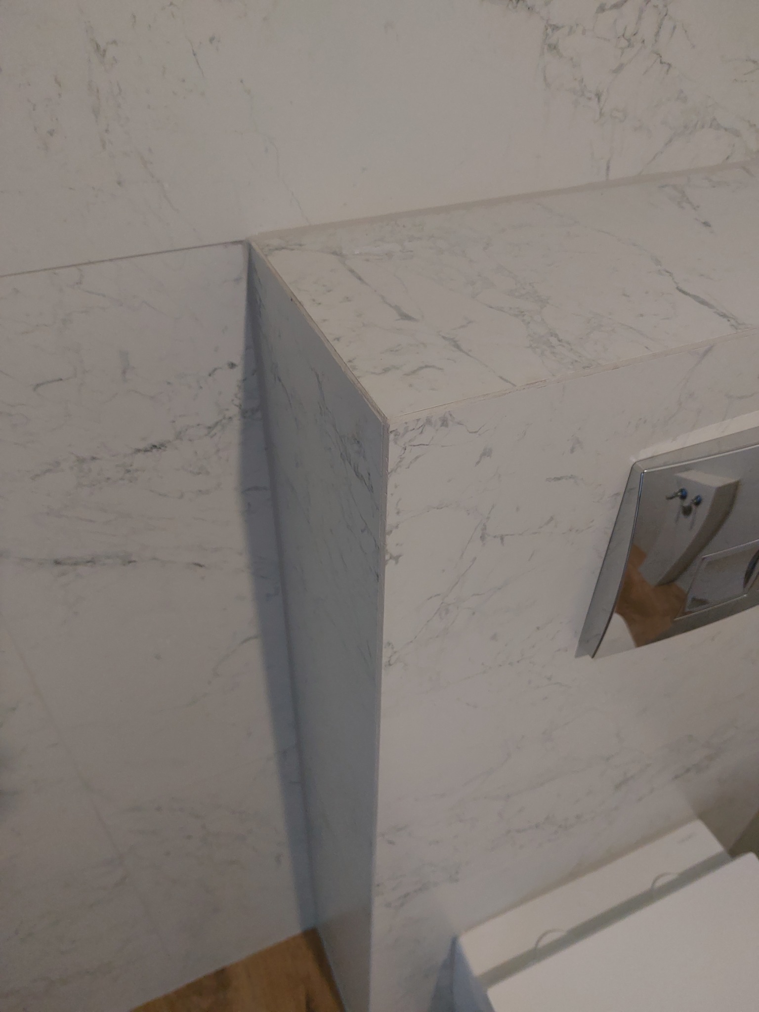 Wykończenie łazienki z płytkami imitującymi marmur. Widoczny fragment zabudowy stelaża WC z przyciskiem. Estetyczne połączenie płyt pod kątem 45 stopni.