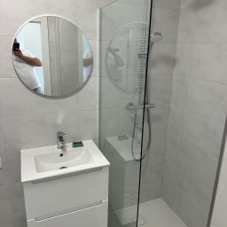 MONTECH SPÓŁKA Z OGRANICZONĄ ODPOWIEDZIALNOŚCIĄ - Nowoczesna łazienka w szarościach: kabina prysznicowa typu walk-in, okrągłe lustro z odbiciem osoby robiącej zdjęcie, biała szafka z umywalką, minimalistyczne oświetlenie.