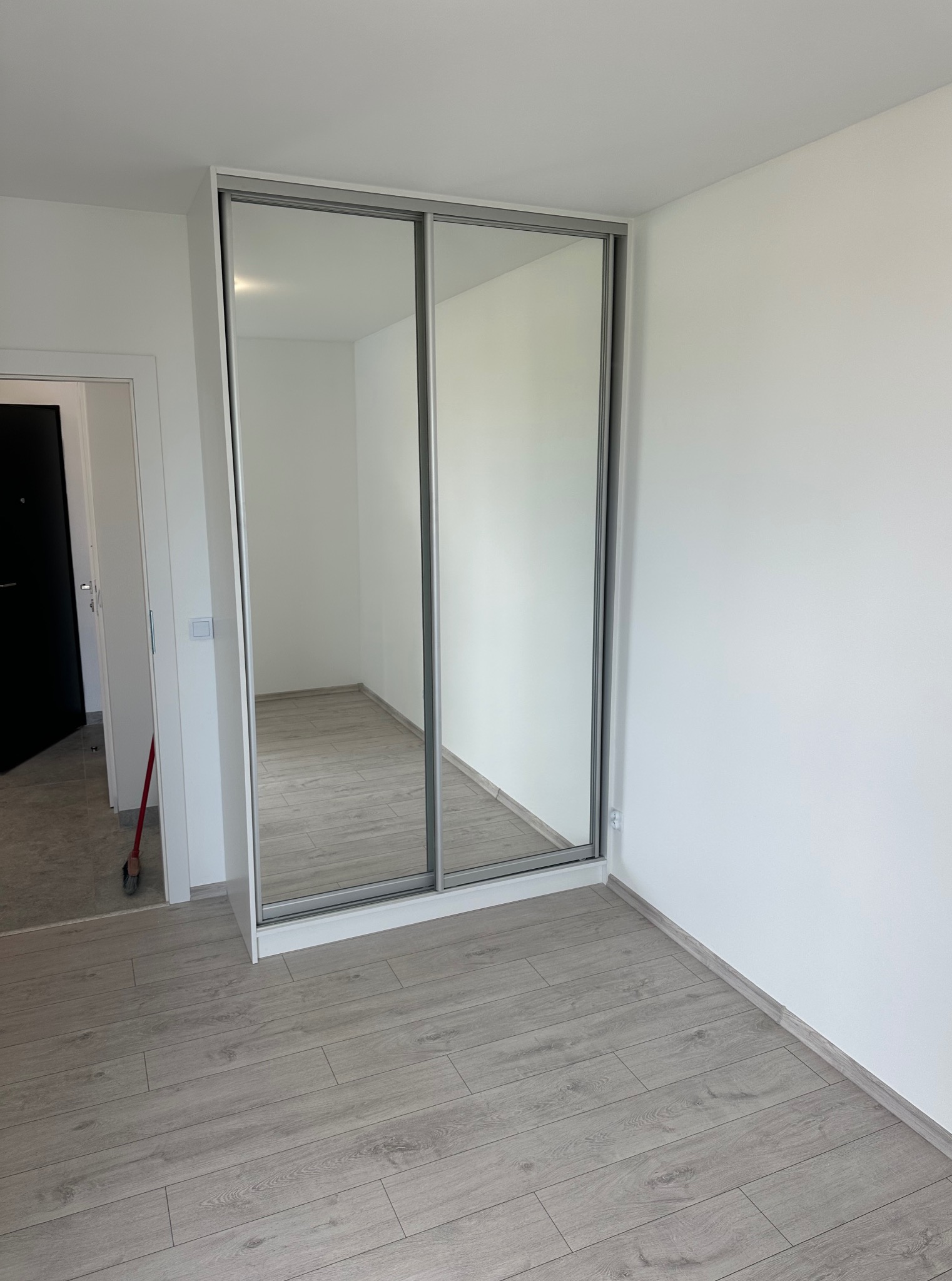 Nowoczesna szafa wnękowa z przesuwnymi drzwiami lustrzanymi w jasnym wnętrzu z panelami podłogowymi. Minimalistyczny design.