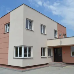 Dwukondygnacyjny budynek otynkowany w kolorach beżowym i łososiowym z białymi oknami PCV, widok z zewnątrz w słoneczny dzień.