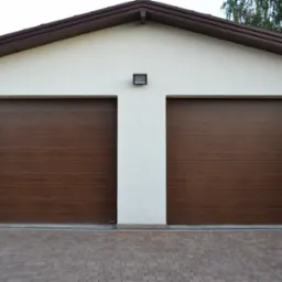 Dwie brązowe segmentowe bramy garażowe w jasnym budynku z brązowym dachem i kostką brukową na podjeździe.