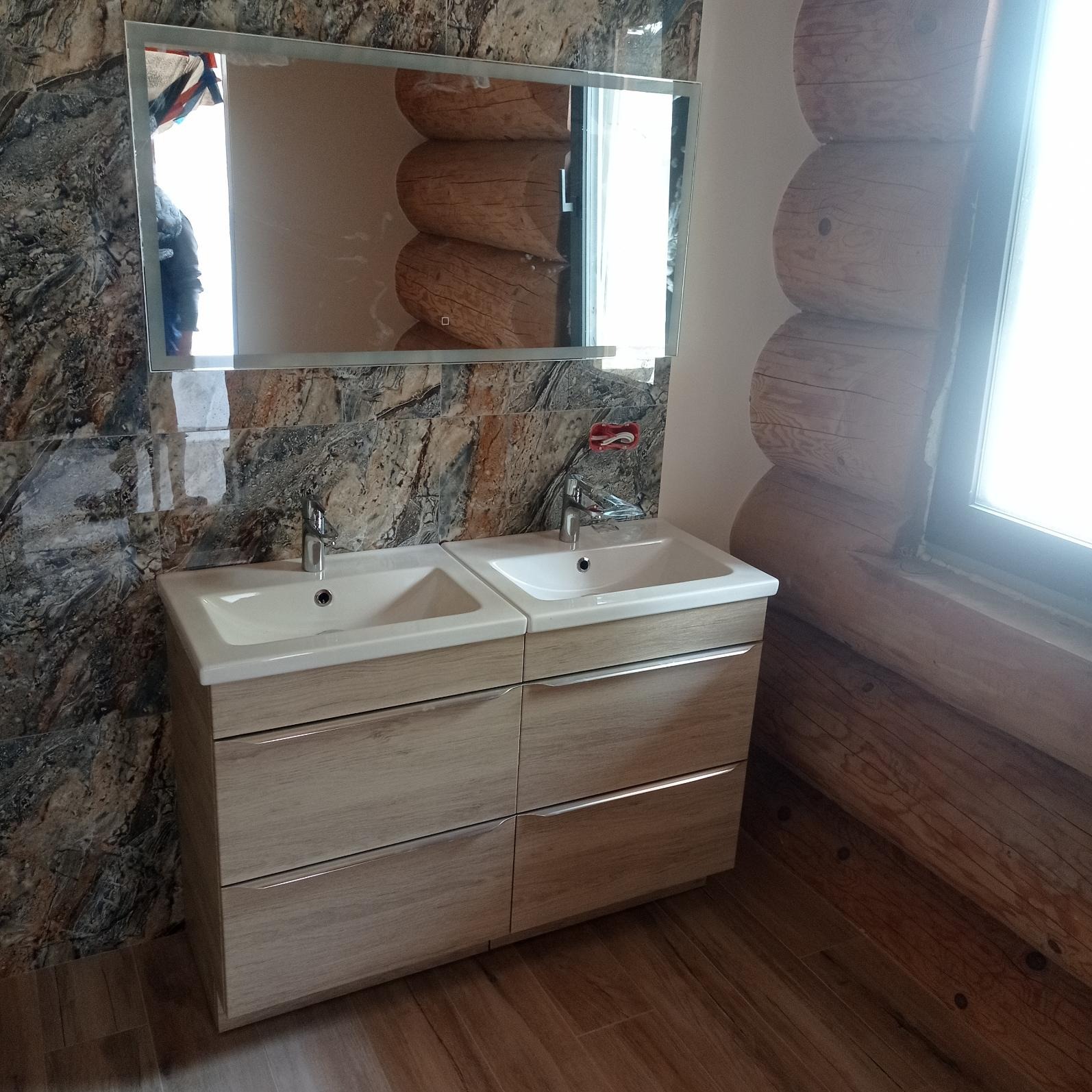 Nowoczesna łazienka w stylu rustykalnym z podwójną umywalką nablatową na szafce z drewnianymi frontami, lustro w srebrnej ramie odbija fragment drewnianej ściany, marmurowe płytki na ścianie po...