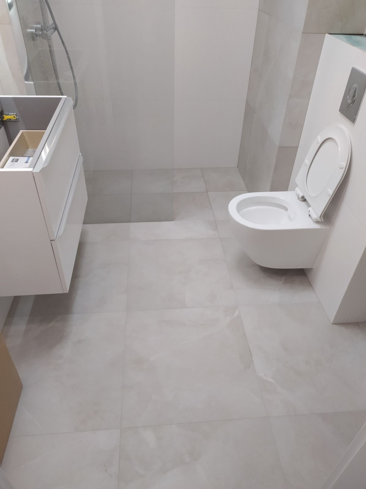 Nowoczesna łazienka z wiszącą toaletą, szafką pod umywalkę i kabiną prysznicową, wykończona płytkami imitującymi marmur w odcieniach szarości i bieli.