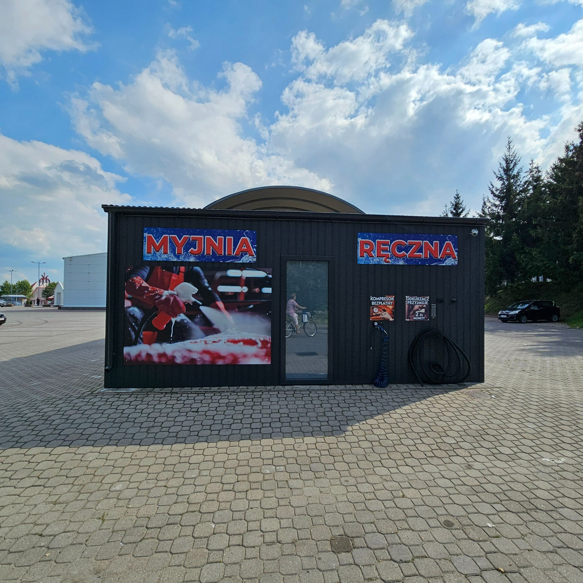 Budynek myjni ręcznej z reklamami na fasadzie, widoczny rowerzysta w odbiciu szyby