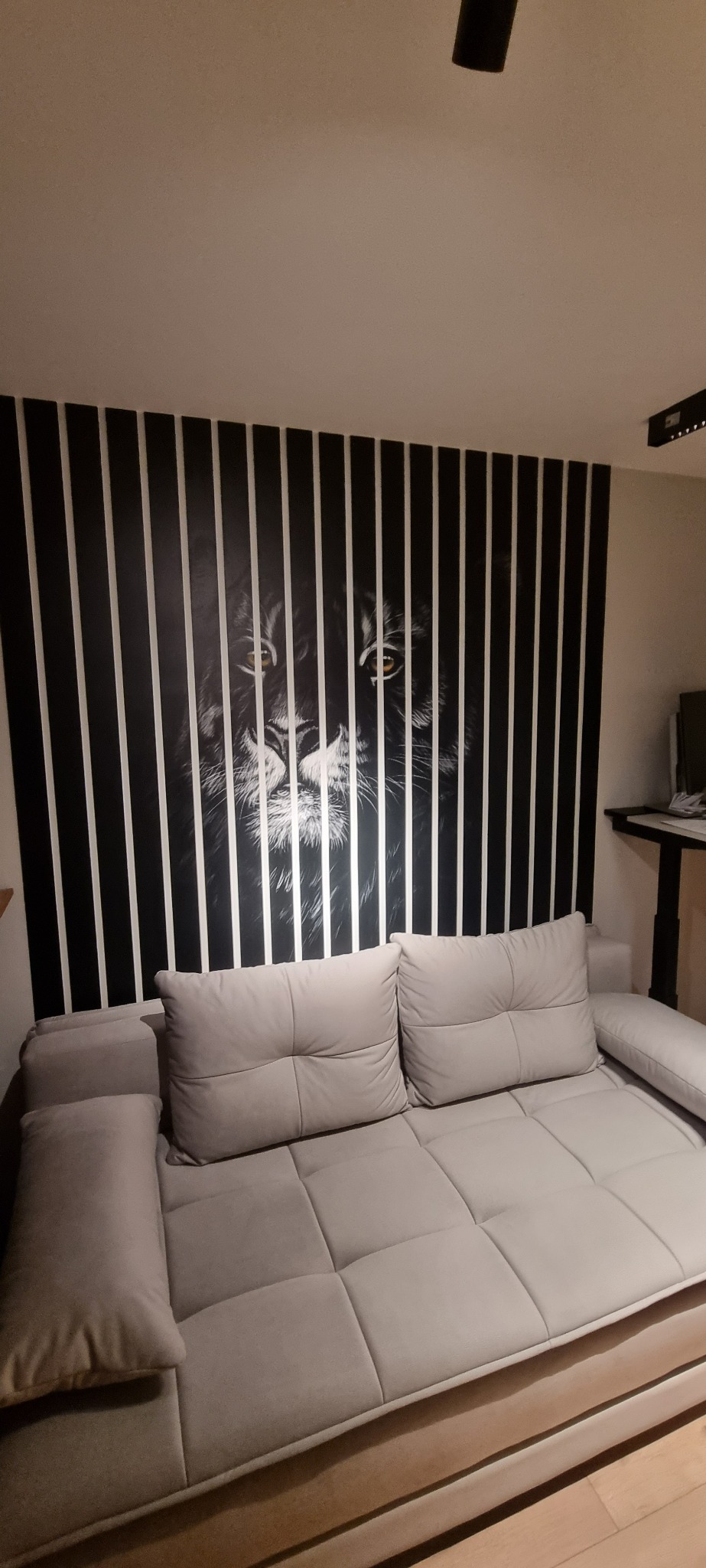 Salon z szarą sofą i dekoracją ścienną przedstawiającą lwa za czarno-białymi pasami.