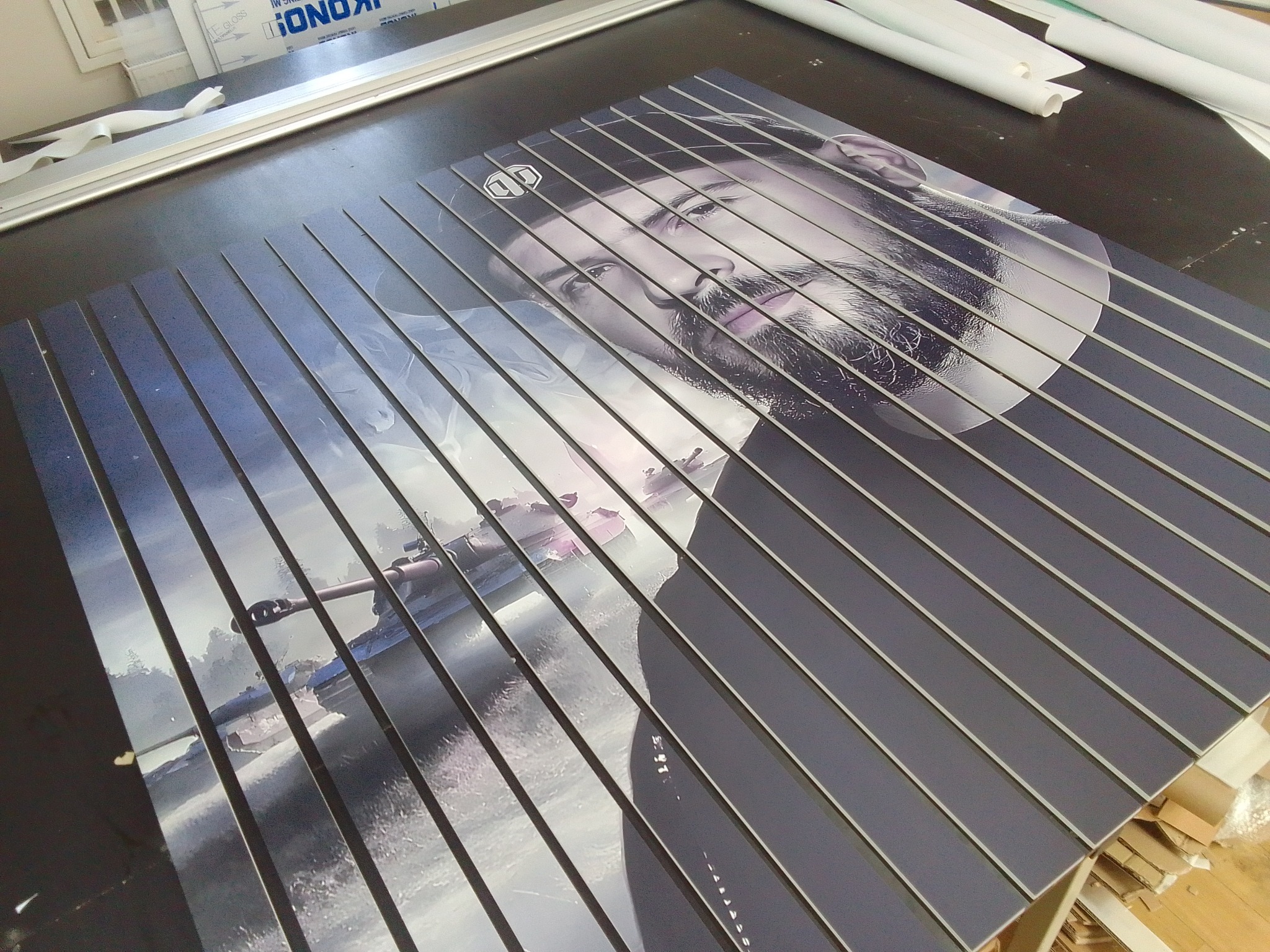 Wydrukowane panele z wizerunkiem mężczyzny w czapce i czołgu, pocięte na paski i ułożone obok siebie, gotowe do montażu.