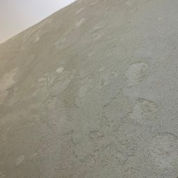 Twoja Ekipa Remontowa Konrad Lewicki - Szara ściana z dekoracyjną, chropowatą fakturą, oświetlona od góry, ukazująca unikalny wzór na powierzchni. Widok pod kątem.