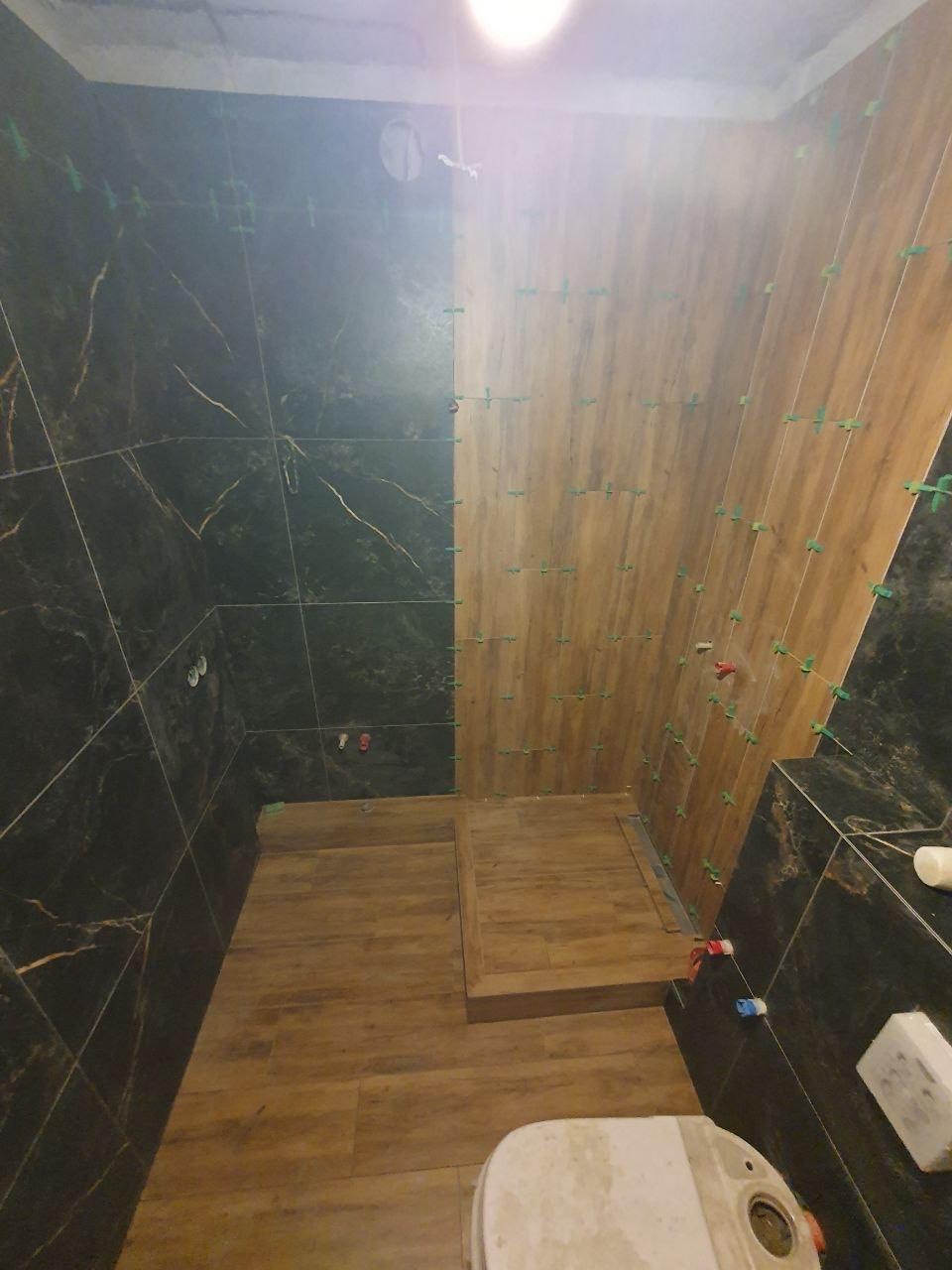 Układanie płytek w łazience: brązowe płytki imitujące drewno na podłodze i ścianie, kontrastujące z czarnymi płytkami z marmurowym wzorem. Widoczne krzyżyki dystansowe.