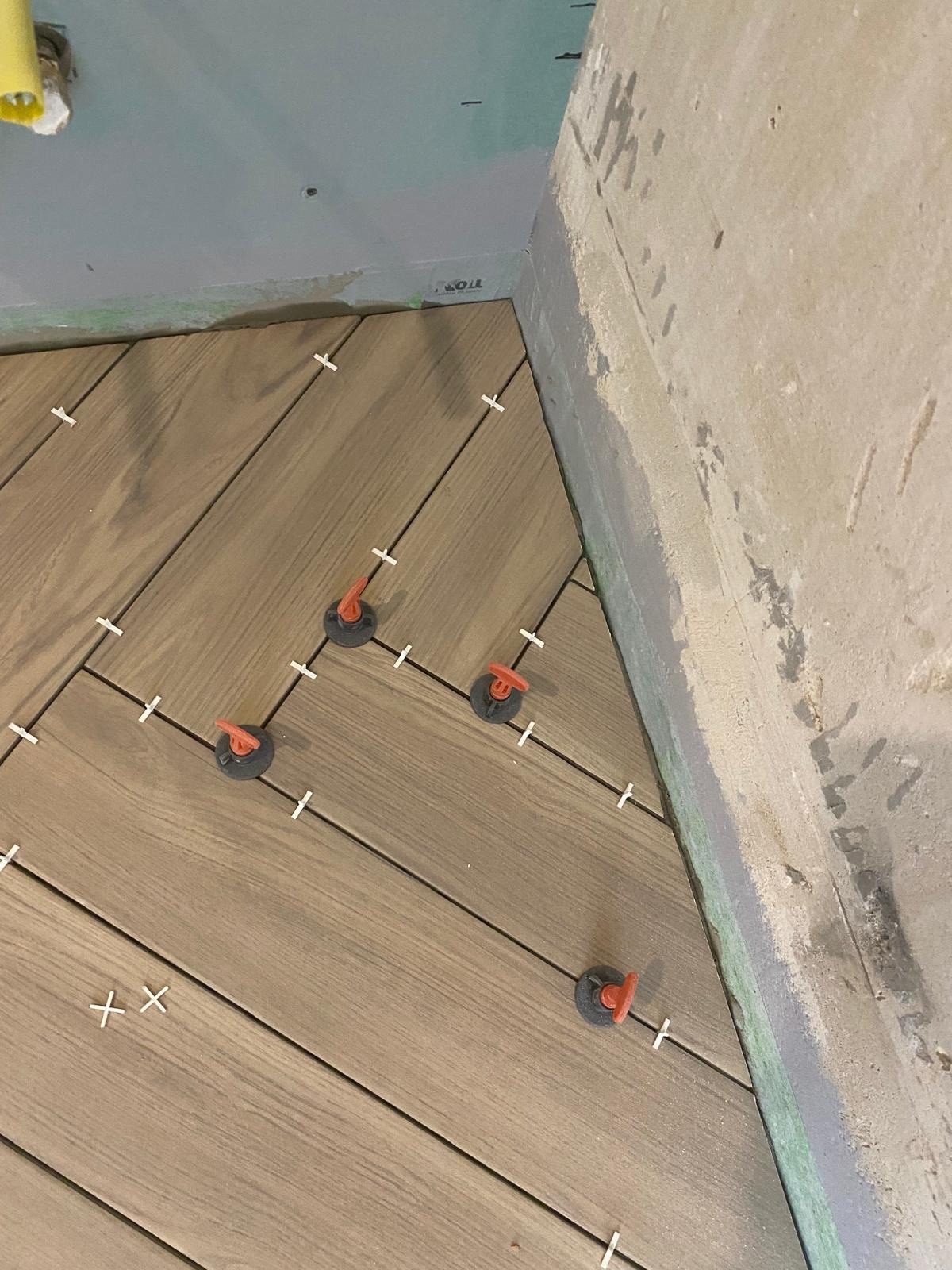 Układanie płytek podłogowych w Ksawerowie z użyciem systemu poziomowania. Widoczne krzyżyki dystansowe i klipsy. Ściana surowa, przygotowana do dalszych prac.