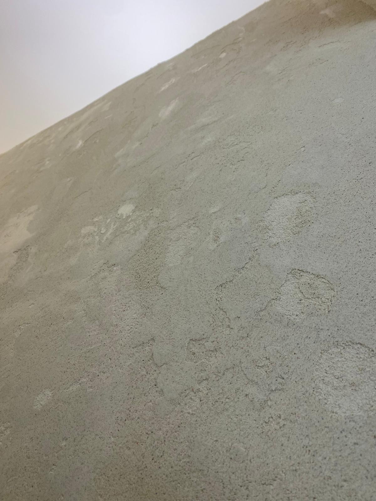 Szara ściana z dekoracyjną, chropowatą fakturą, oświetlona od góry, ukazująca unikalny wzór na powierzchni. Widok pod kątem.