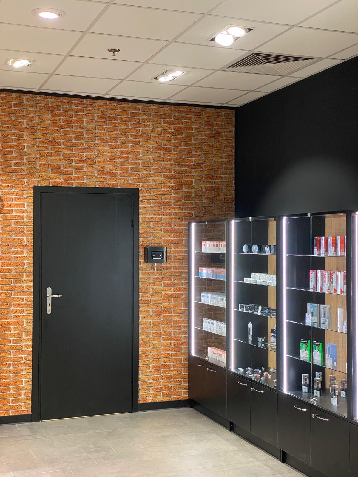 Wykończone wnętrze sklepu z ceglaną ścianą, czarnymi meblami ekspozycyjnymi z oświetleniem LED i czarnymi drzwiami. Nowoczesny design.