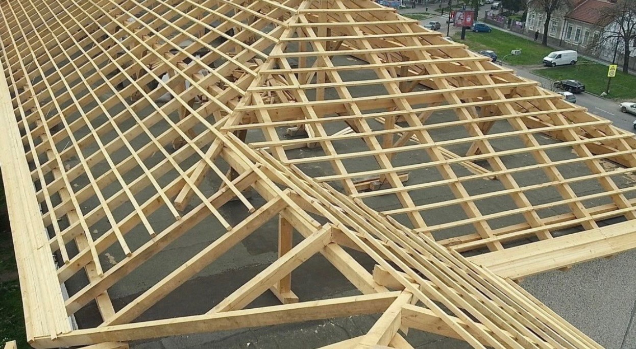 Konstrukcja drewniana dachu w trakcie budowy, widok z góry na ulice miasta w tle.