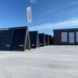 Ekspozycja różnorodnych modeli pokryć dachowych w Lubieniu Kujawskim, prezentowanych na stojakach przed budynkiem. Widoczne dachówki w odcieniach szarości i czerni, z wyraźną fakturą. W tle budynek...