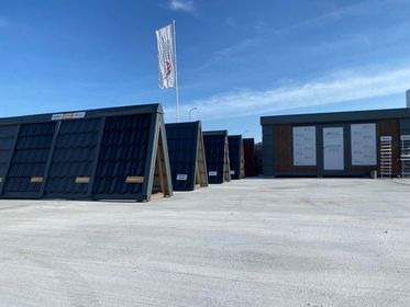 Ekspozycja różnorodnych modeli pokryć dachowych w Lubieniu Kujawskim, prezentowanych na stojakach przed budynkiem. Widoczne dachówki w odcieniach szarości i czerni, z wyraźną fakturą. W tle budynek...