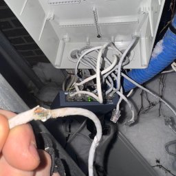 MAŁGORZATA SOBOCIŃSKA - Uszkodzony kabel sieciowy w skrzynce przyłączeniowej, widoczne żyły, obok switch i kable RJ45. Ślady śniegu sugerują montaż na zewnątrz.