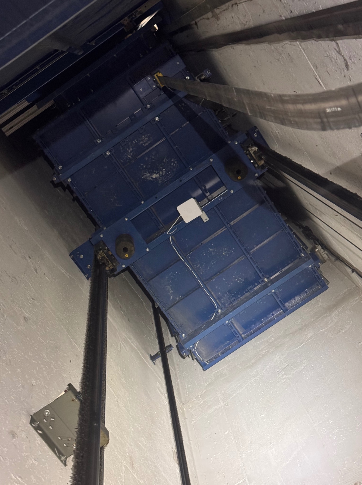 Wnętrze szybu windy z widoczną platformą serwisową, oświetleniem i elementami konstrukcyjnymi. Perspektywa z dołu, ukazująca detale techniczne i przestrzeń roboczą.