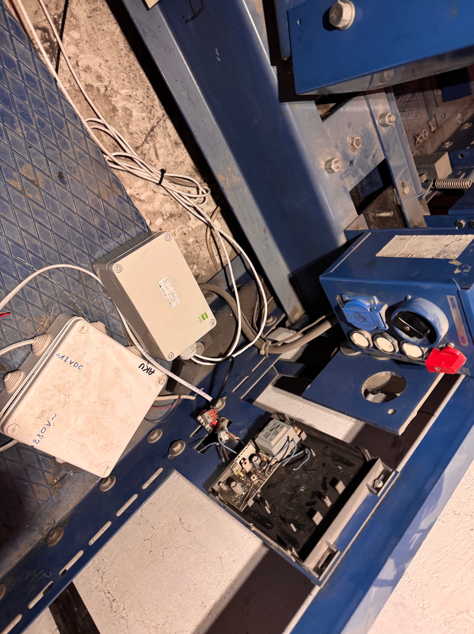 Niebieska metalowa konstrukcja z puszkami elektrycznymi, przewodami i elementami sterującymi. Widoczne złącza, transformator i płytka drukowana.