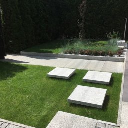 GRANITEK Marek Żoch - Nowoczesny ogród z kwadratowymi płytami chodnikowymi z jasnoszarego kamienia ułożonymi na trawniku, obrzeża z kostki granitowej i wysokie tuje w tle.