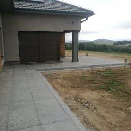 GRANITEK Marek Żoch - Szara, kamienna ścieżka prowadząca do tarasu z płyt granitowych, z widokiem na krajobraz pagórkowaty w tle, w pochmurny dzień.