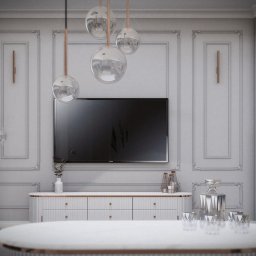 Sebastian Filuś - Nowoczesny salon z telewizorem na ścianie z dekoracyjnymi panelami, wiszące szklane lampy, biała komoda i okrągły stolik kawowy z marmurowym blatem.