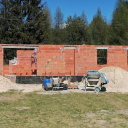 Osoba prywatna - Wznoszenie ścian z czerwonej cegły na budowie domu w Lutomiersku. Widoczna betoniarka, piasek i narzędzia murarskie.