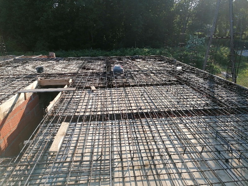 Zbrojenie stropu z siatki stalowej i betonowych podkładek dystansowych, widoczne elementy deskowania i fragment murowanej ściany z pustaków.