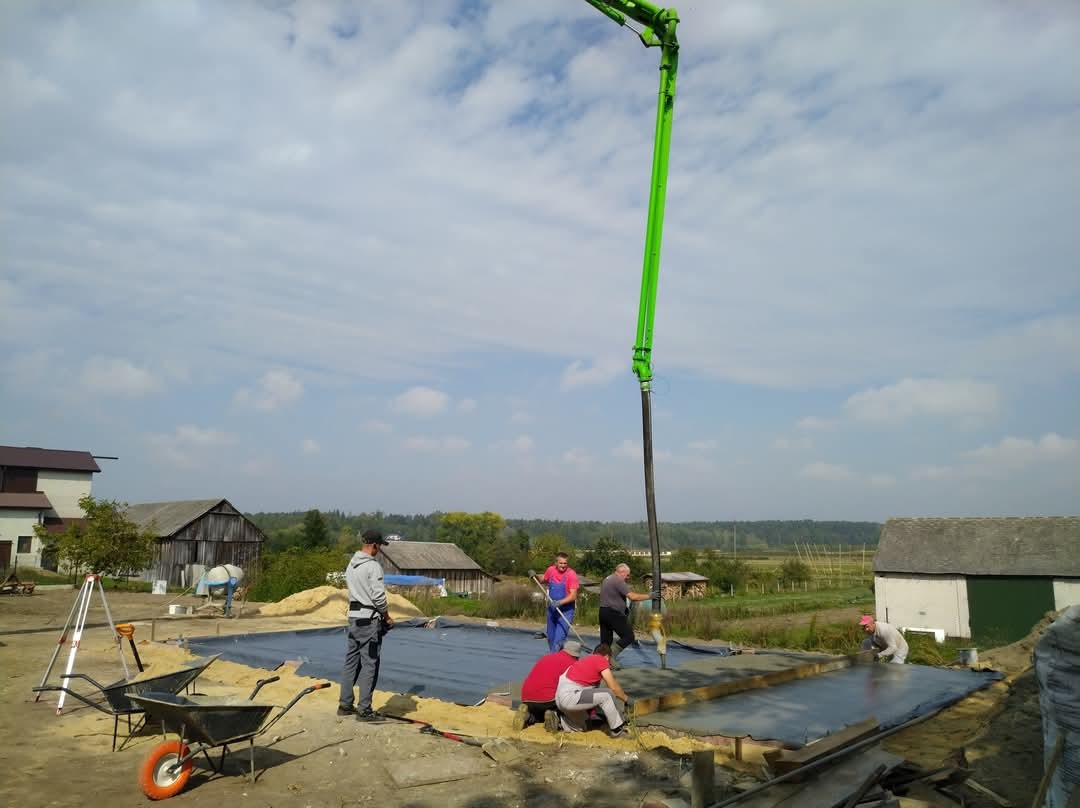 Wylewanie fundamentów pod budynek jednorodzinny za pomocą pompy do betonu; widoczny szalunek i ekipa pracowników w trakcie prac.