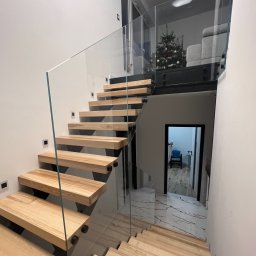 CNL Tomasz Pietrucha - Nowoczesne schody drewniane z balustradą szklaną, mocowane punktowo, z widocznym fragmentem świątecznej choinki w tle.