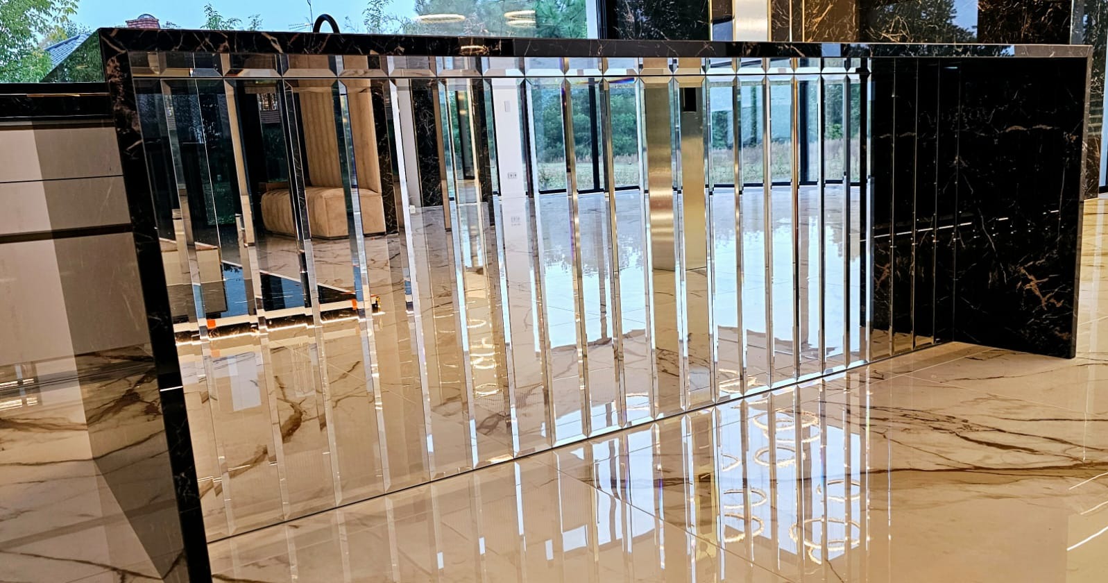 Nowoczesna wyspa kuchenna z frontem z pionowych, lustrzanych paneli, wykończona czarnym marmurem, odbijająca światło na polerowanej podłodze z marmuru.