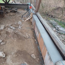 Bartek-Bruk - Wylewka betonowa w szalunku z desek i cegieł, teren przygotowany pod budowę, widoczne narzędzia i maszyny budowlane. Prace ziemne w toku.