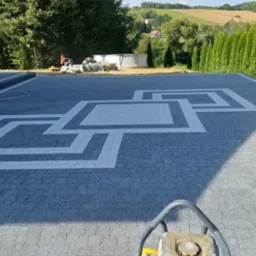 Ułożona kostka brukowa z geometrycznym wzorem w Jodłowej, widok z góry z wibratorem do zagęszczania. W tle zielony krajobraz.