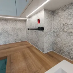 Fragment łazienki w trakcie prac wykończeniowych: ułożone płytki z wzorem, drewnopodobny blat, widoczne gniazdko elektryczne w ścianie i oświetlenie LED podszafkowe.