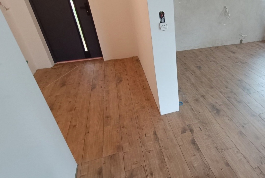 Ułożona podłoga z paneli imitujących drewno w Bielsku Podlaskim, widoczna instalacja elektryczna w ścianie, ściany przygotowane do dalszych prac wykończeniowych.