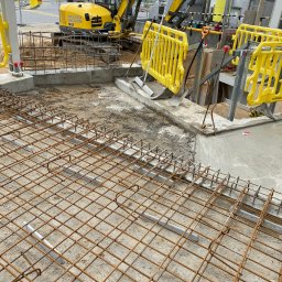 Usługi hydrauliczne wod-kan - Przygotowanie podłoża pod wylewkę betonową z widoczną siatką zbrojeniową i żółtym mini-koparką Wacker Neuson w tle.