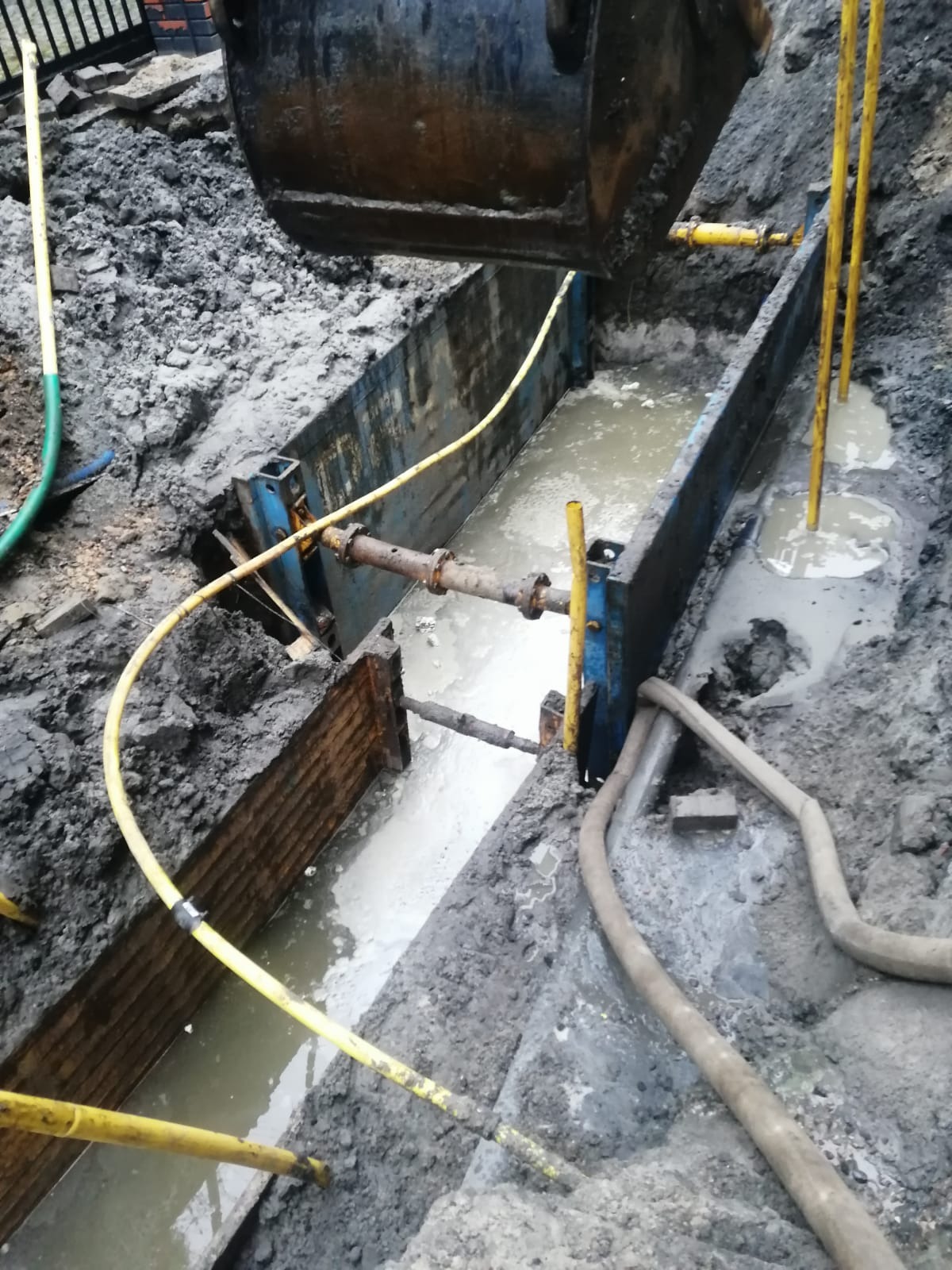 Wykop zabezpieczony szalunkiem stalowym, wypełniony wodą i błotem, widoczne rury i węże w Wyszkowie.