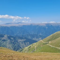 Iwona Sieluk Terapia - Olsztyńskie Centrum Terapii TSR Punkt Zwrotny - Panoramiczny widok na góry z krętymi ścieżkami i osadą na zboczu, błękitne niebo z białymi obłokami w tle.