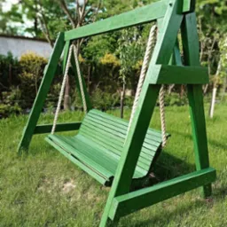 Drewniana huśtawka ogrodowa, pomalowana na zielono, zawieszona na grubych, plecionych linach, ustawiona na trawniku w słoneczny dzień. Widoczne ślady pędzla na drewnie.