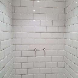 GAB Home Improvements - Ściana w łazience wyłożona białymi, prostokątnymi płytkami typu metro, z widocznymi dwoma wyprowadzonymi rurami instalacji wodnej.